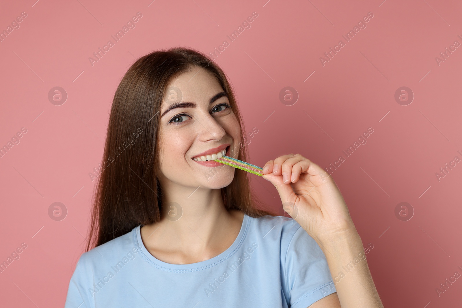 Photo of Young woman eating tasty rainbow sour belt on pink background