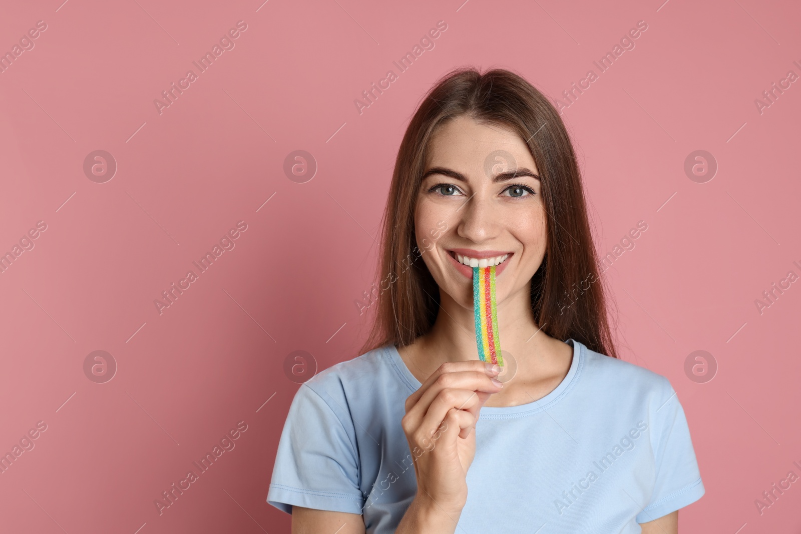 Photo of Young woman eating tasty rainbow sour belt on pink background