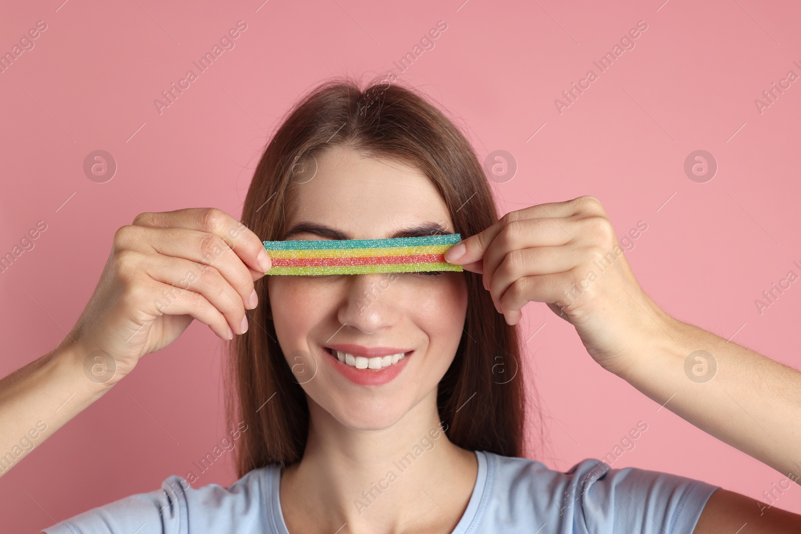 Photo of Happy young woman closing her eyes with tasty rainbow sour belt on pink background