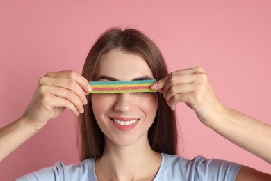 Photo of Happy young woman closing her eyes with tasty rainbow sour belt on pink background