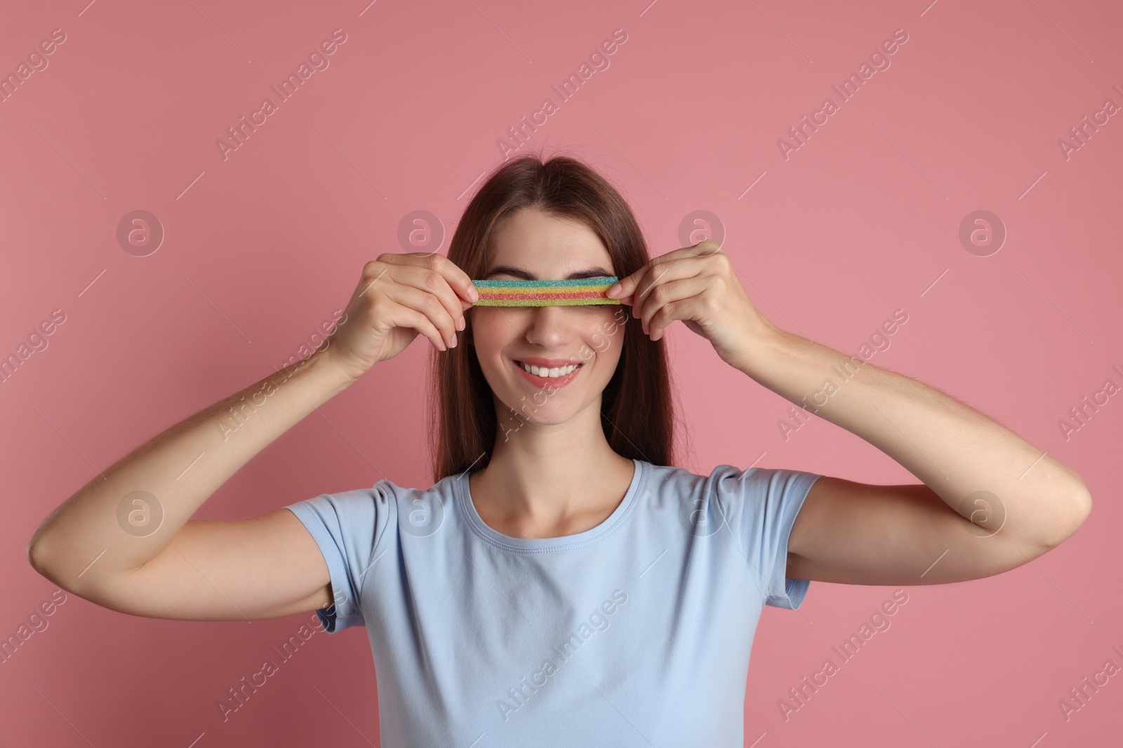 Photo of Happy young woman closing her eyes with tasty rainbow sour belt on pink background