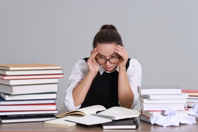 Photo of Young student having stress before exam at desk against grey background