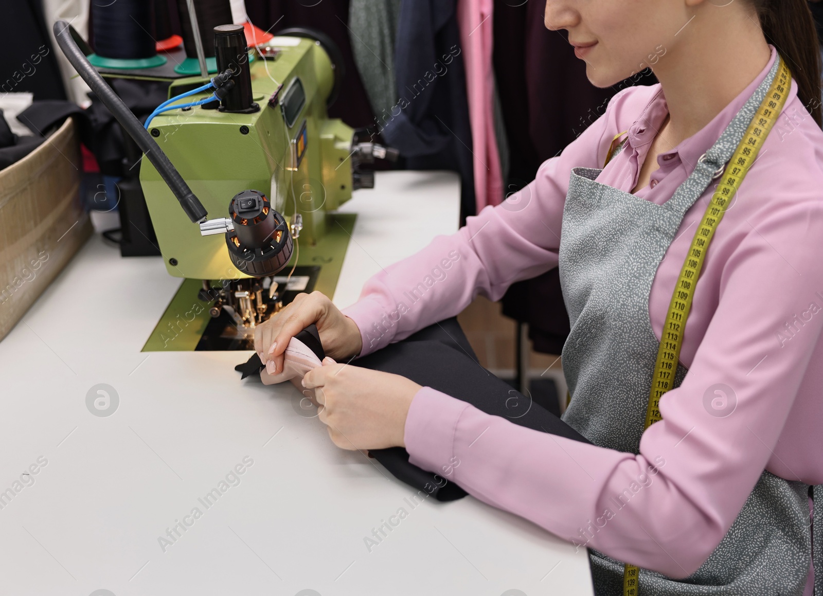 Photo of Young woman working with sewing machine in professional workshop, closeup