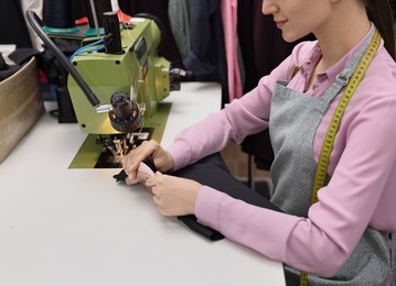 Photo of Young woman working with sewing machine in professional workshop, closeup