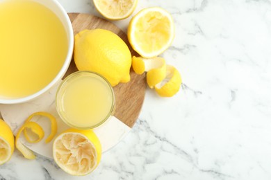 Photo of Fresh lemon juice and squeezed fruits on white marble table, flat lay. Space for text