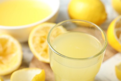 Photo of Glass of fresh lemon juice and squeezed fruits on table, closeup