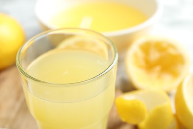 Photo of Glass of fresh lemon juice and squeezed fruits on table, closeup