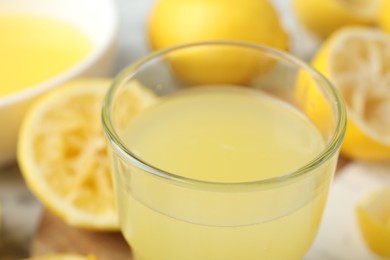 Photo of Glass of fresh lemon juice and squeezed fruits on table, closeup