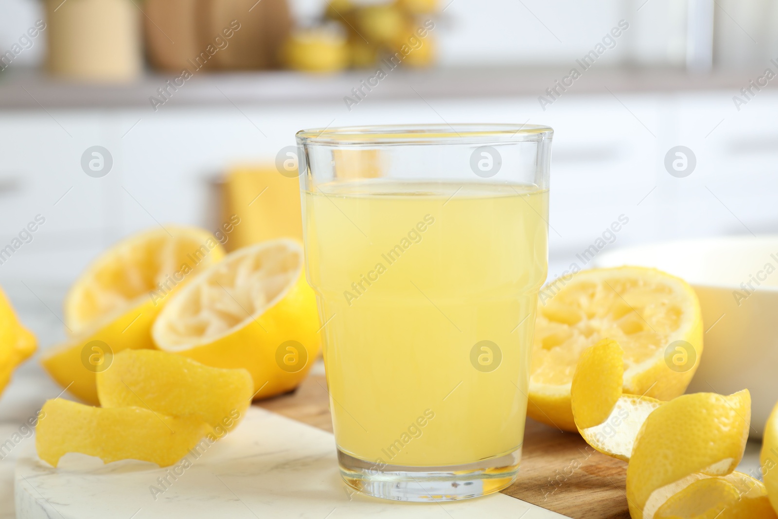 Photo of Glass of fresh lemon juice and squeezed fruits on table, closeup