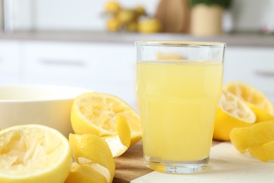 Photo of Glass of fresh lemon juice and squeezed fruits on table, closeup