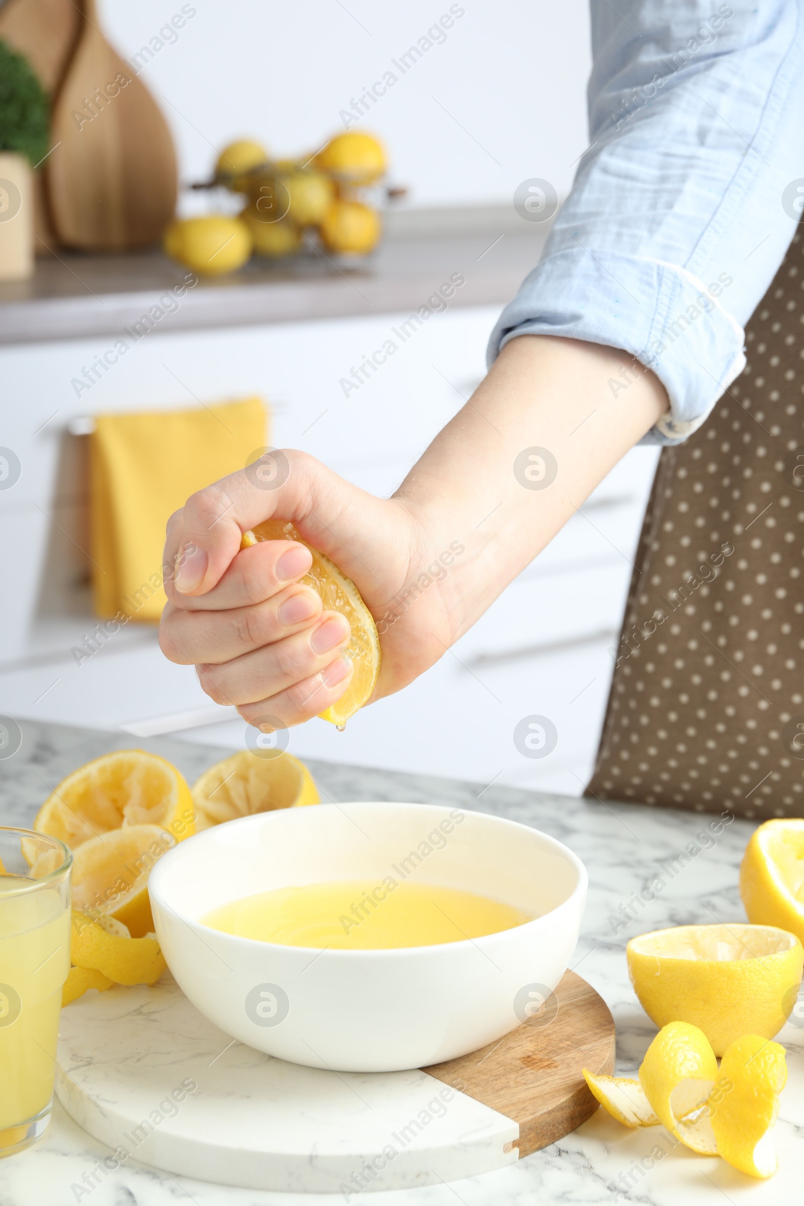 Photo of Woman squeezing lemon juice into bowl at marble table, closeup