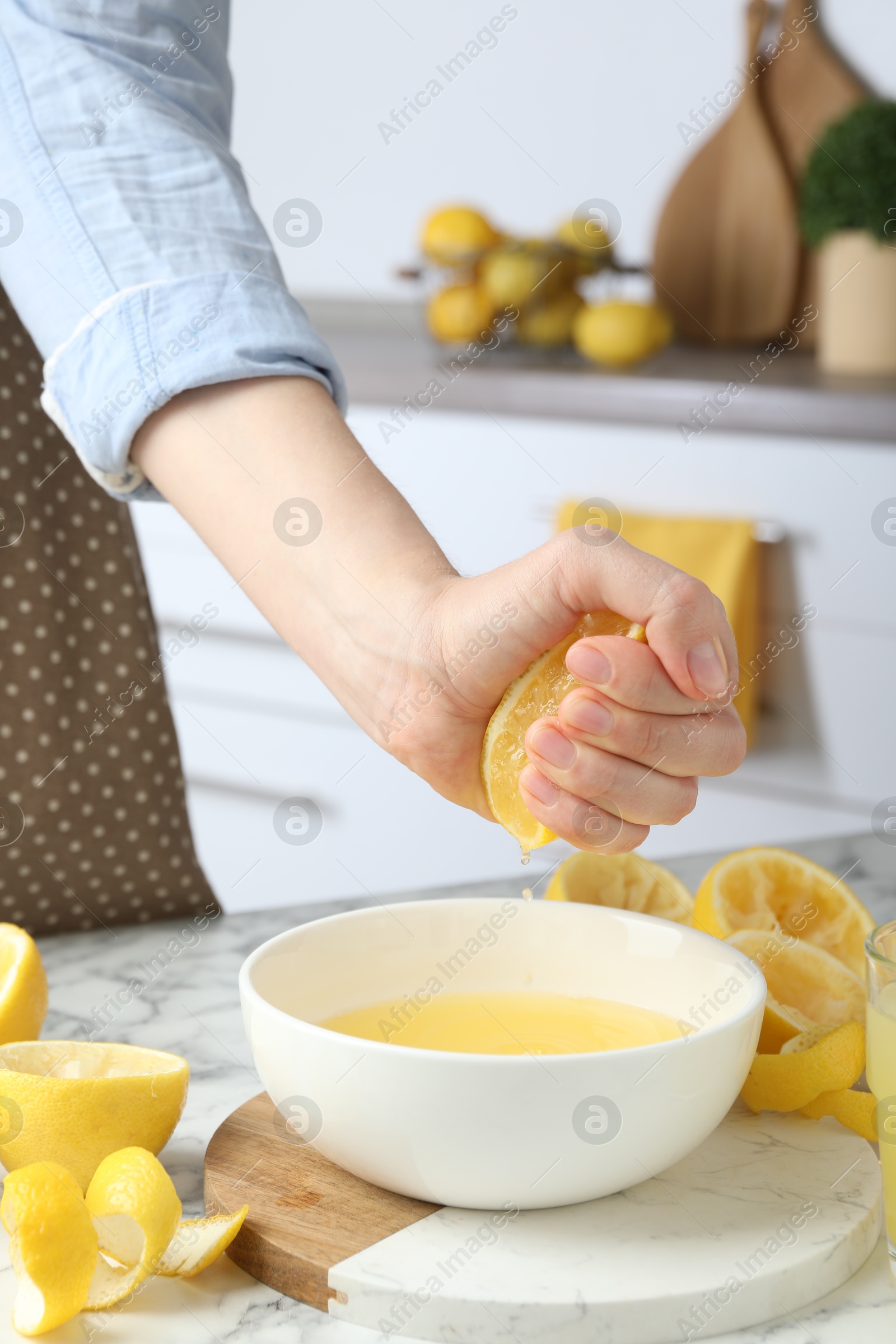 Photo of Woman squeezing lemon juice into bowl at marble table, closeup