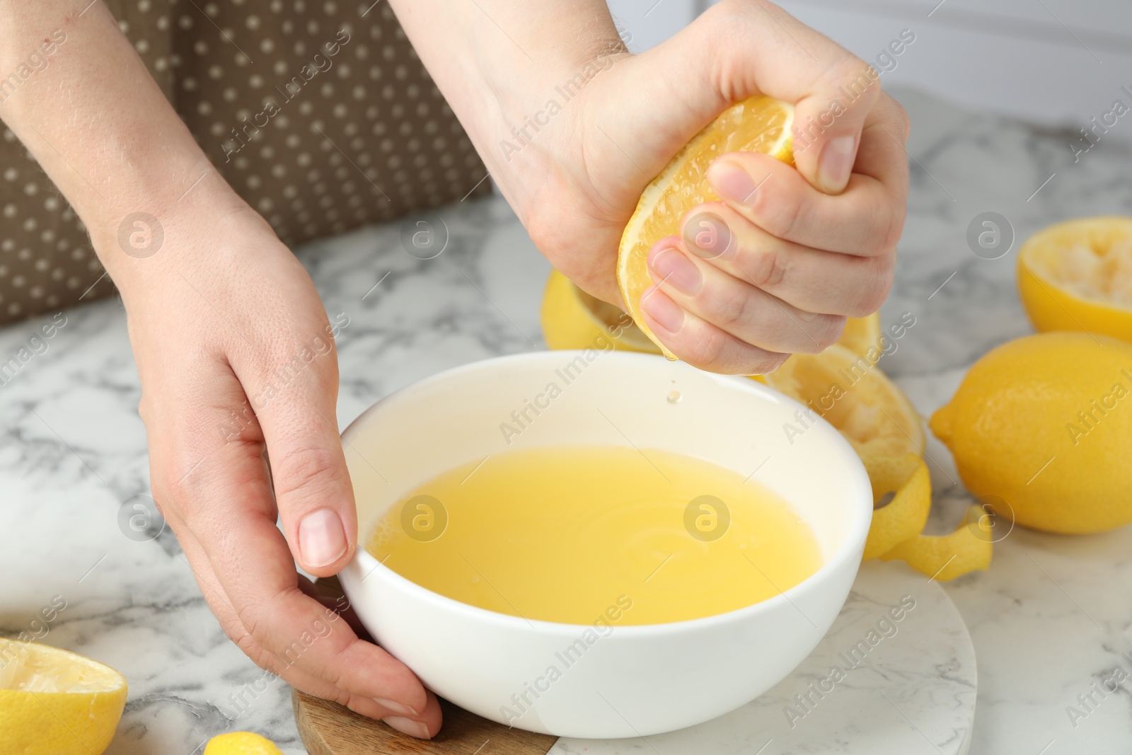 Photo of Woman squeezing lemon juice into bowl at marble table, closeup