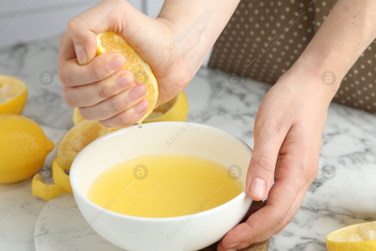 Photo of Woman squeezing lemon juice into bowl at marble table, closeup