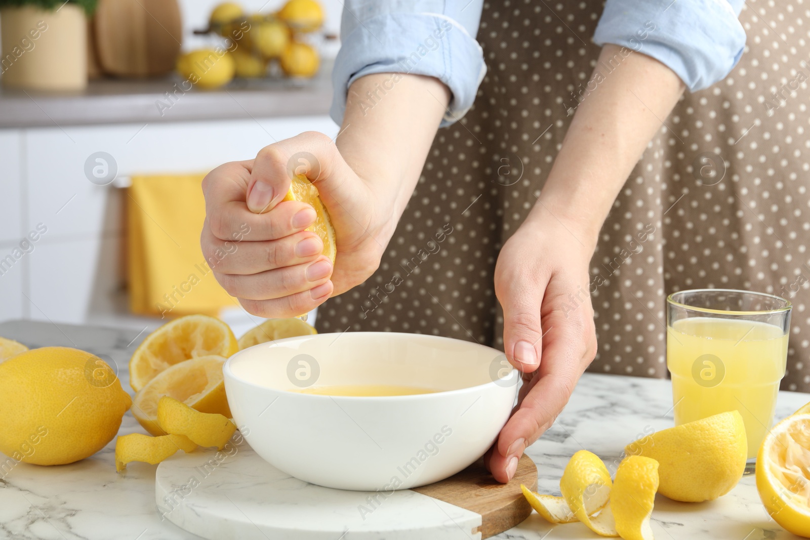 Photo of Woman squeezing lemon juice into bowl at marble table, closeup