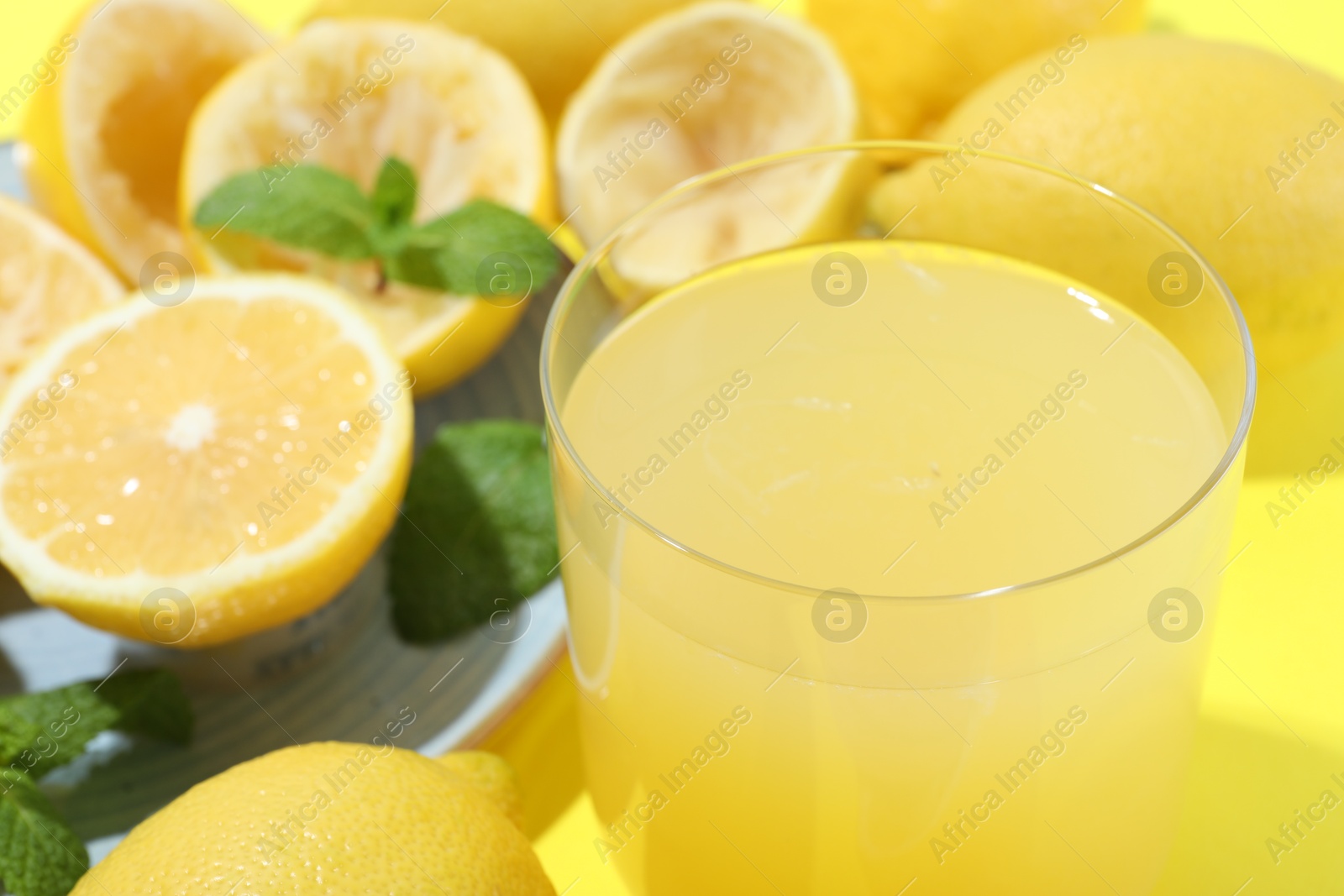 Photo of Glass of fresh lemon juice and squeezed fruits on yellow background, closeup