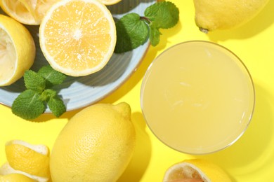 Glass of fresh lemon juice and squeezed fruits on yellow background, flat lay