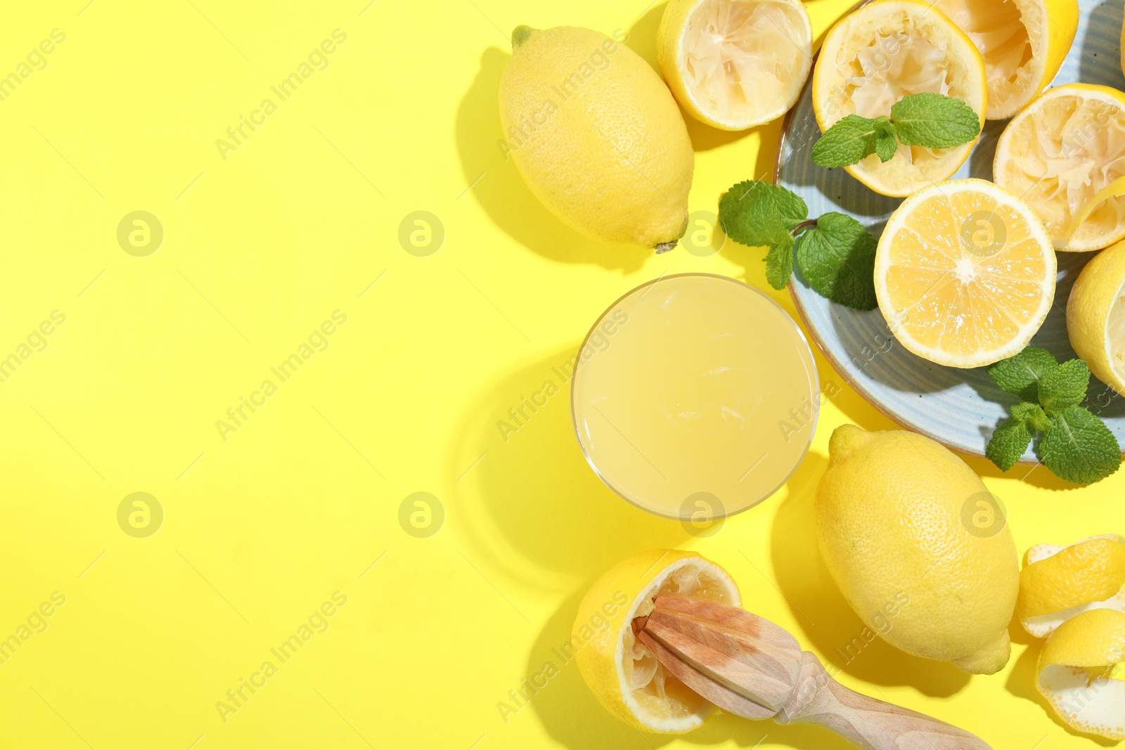 Photo of Glass of fresh lemon juice, squeezer and fruits on yellow background, flat lay. Space for text