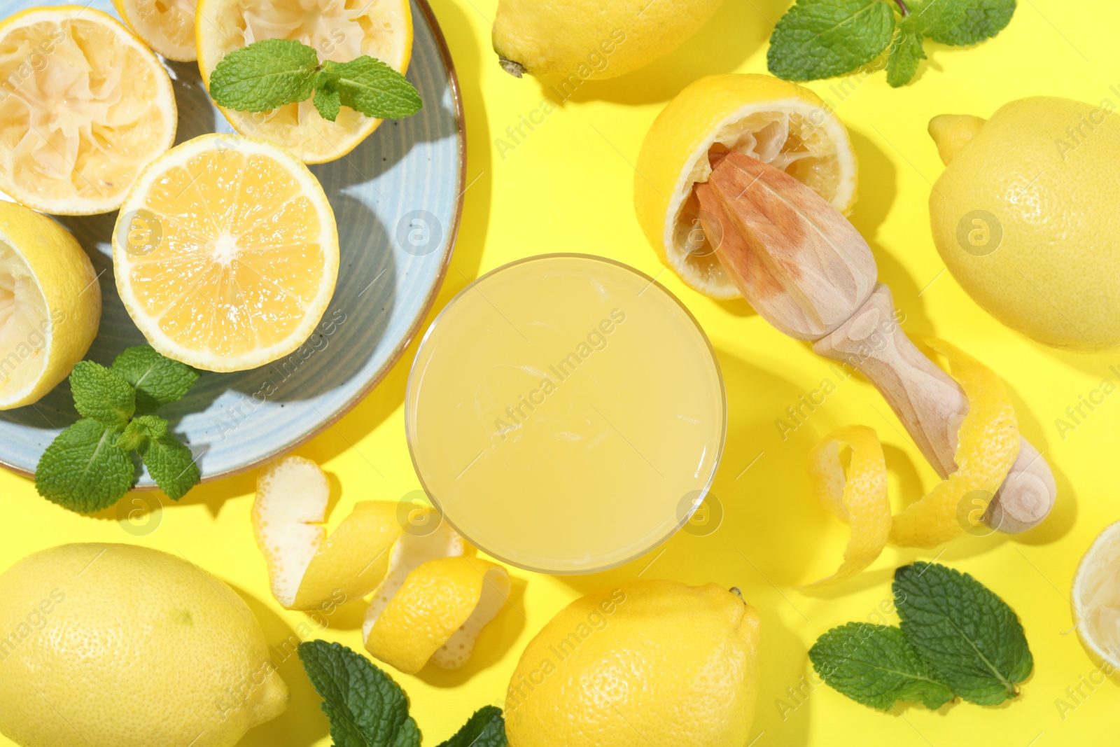 Photo of Glass of fresh lemon juice, squeezer and fruits on yellow background, flat lay