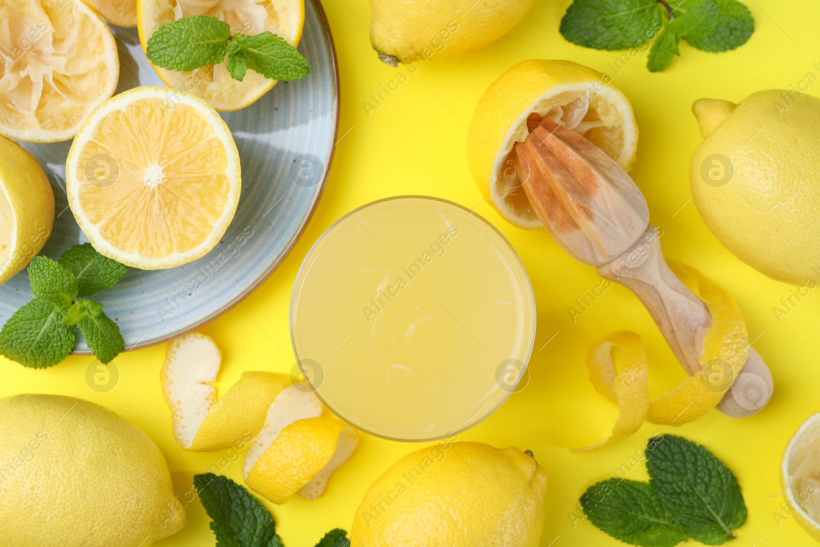 Photo of Glass of fresh lemon juice, squeezer and fruits on yellow background, flat lay