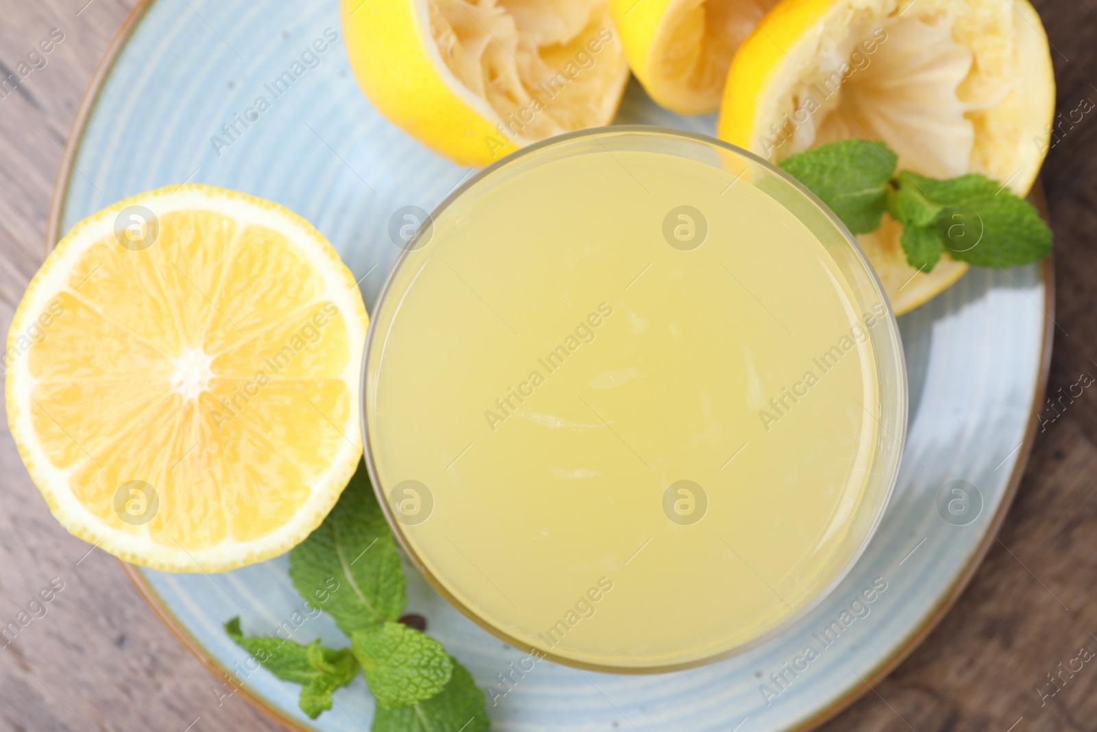 Photo of Glass of lemon juice and fresh fruits on wooden table, top view