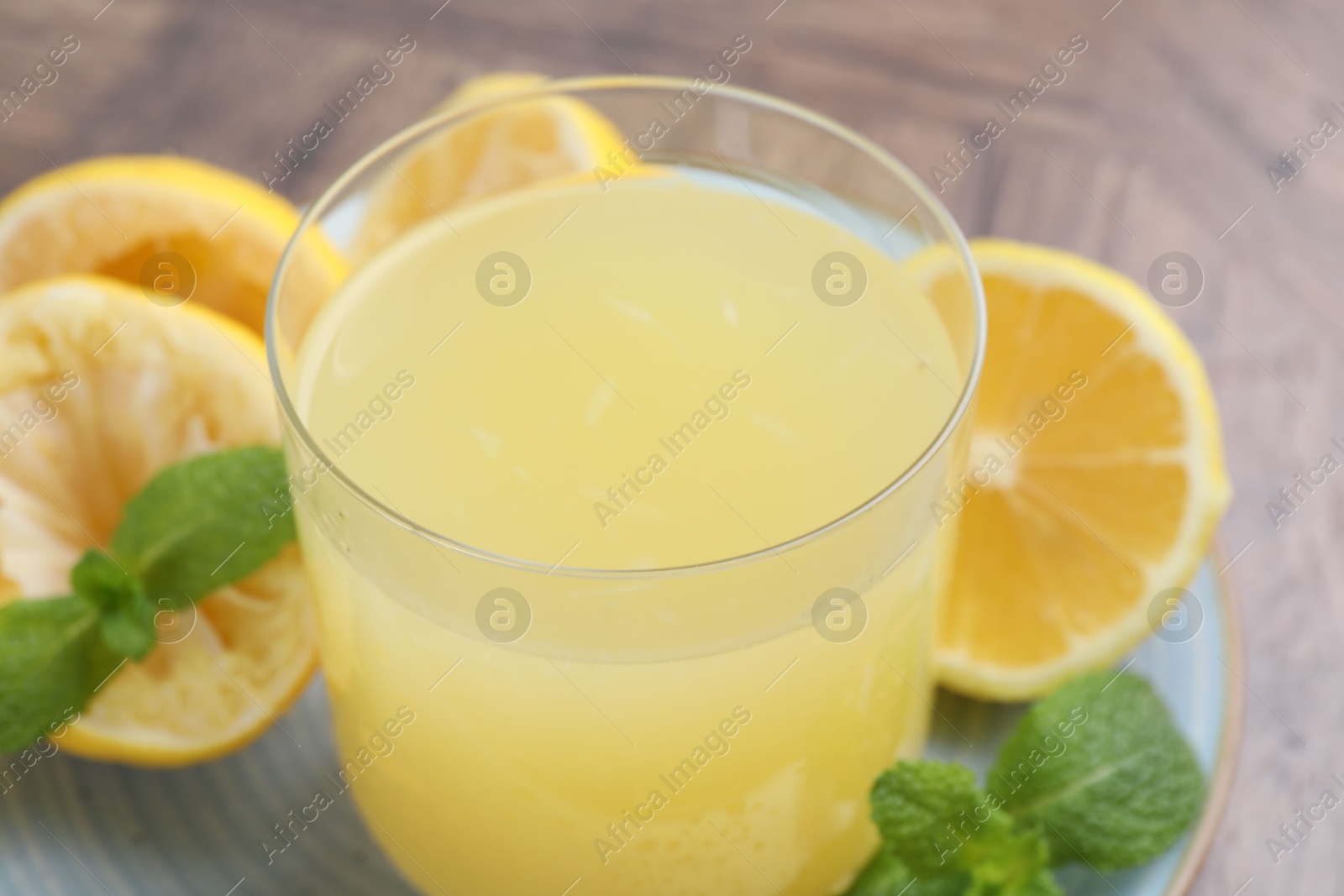 Photo of Glass of lemon juice and fresh fruits on wooden table, closeup