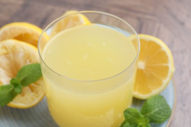 Photo of Glass of lemon juice and fresh fruits on wooden table, closeup