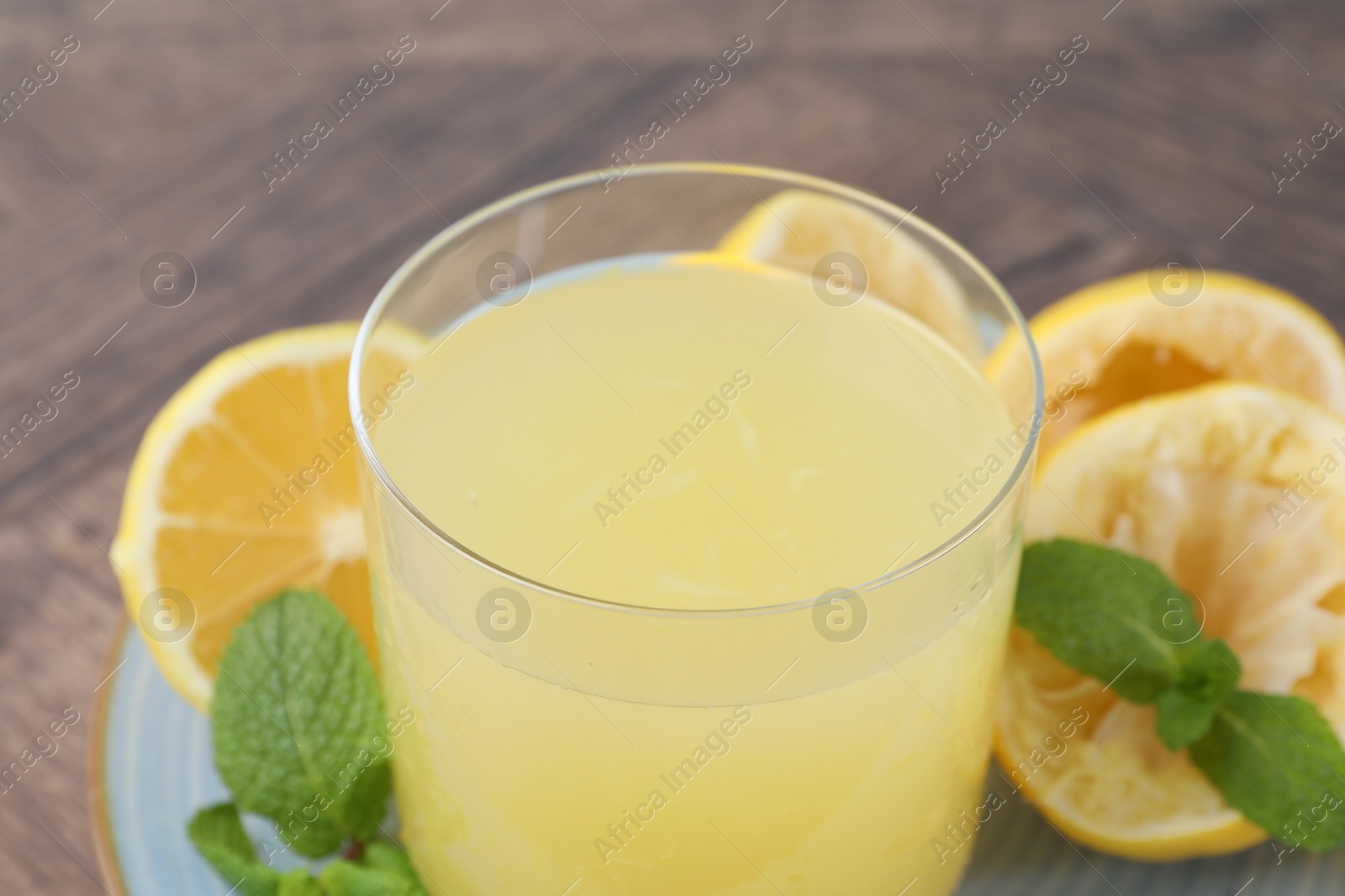 Photo of Glass of lemon juice and fresh fruits on wooden table, closeup