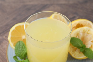 Photo of Glass of lemon juice and fresh fruits on wooden table, closeup