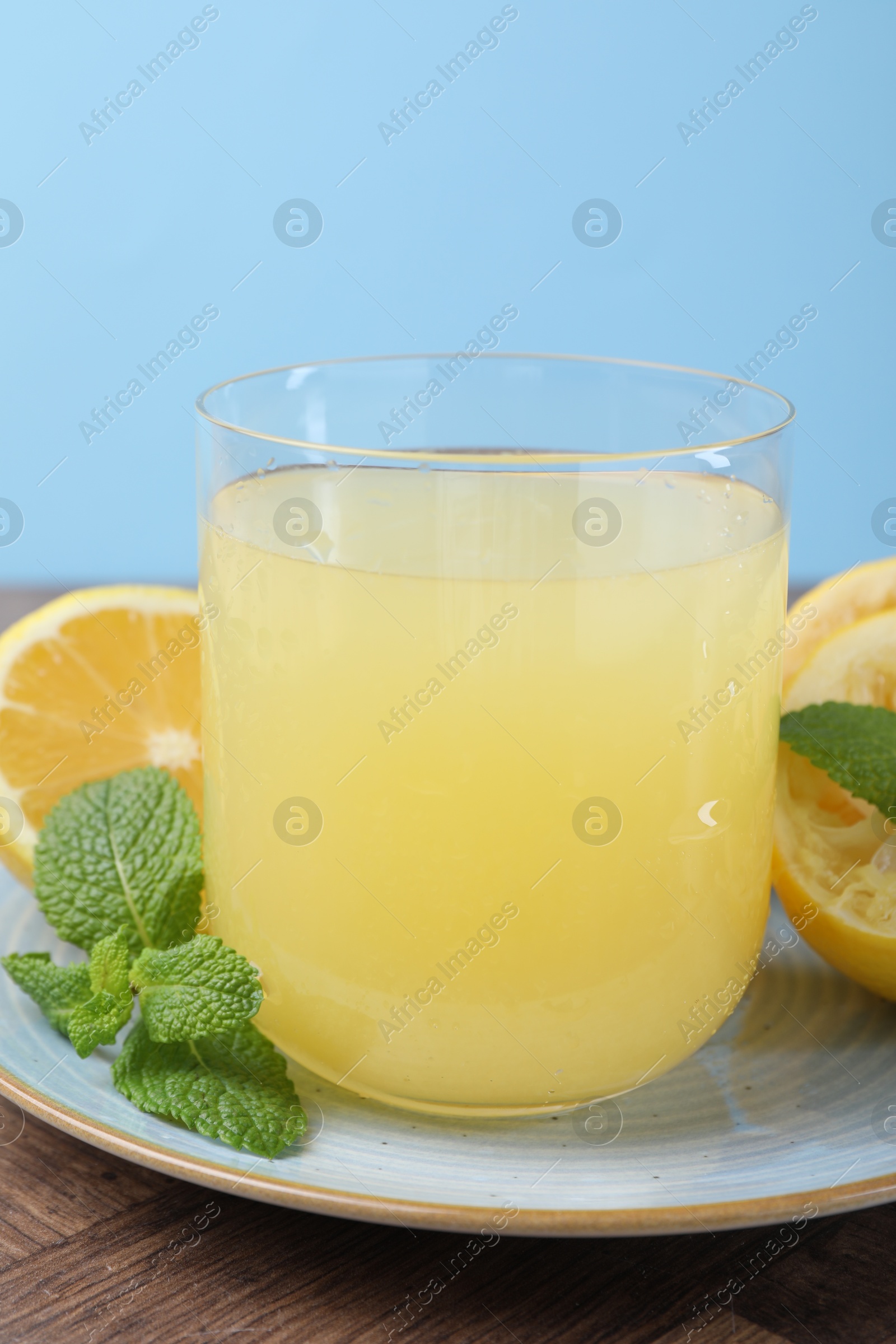 Photo of Glass of lemon juice and fresh fruits on wooden table, closeup