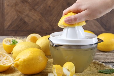 Photo of Woman with lemon using juicer at wooden table, closeup