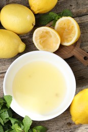 Photo of Fresh lemon juice in bowl and fruits on wooden table, flat lay