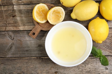 Photo of Fresh lemon juice in bowl and fruits on wooden table, flat lay