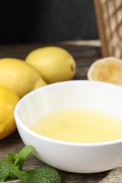 Fresh lemon juice in bowl and fruits on wooden table, closeup