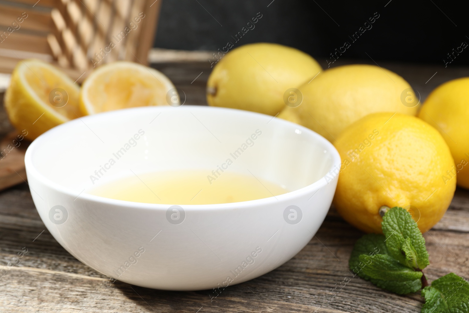 Photo of Fresh lemon juice in bowl and fruits on wooden table, closeup