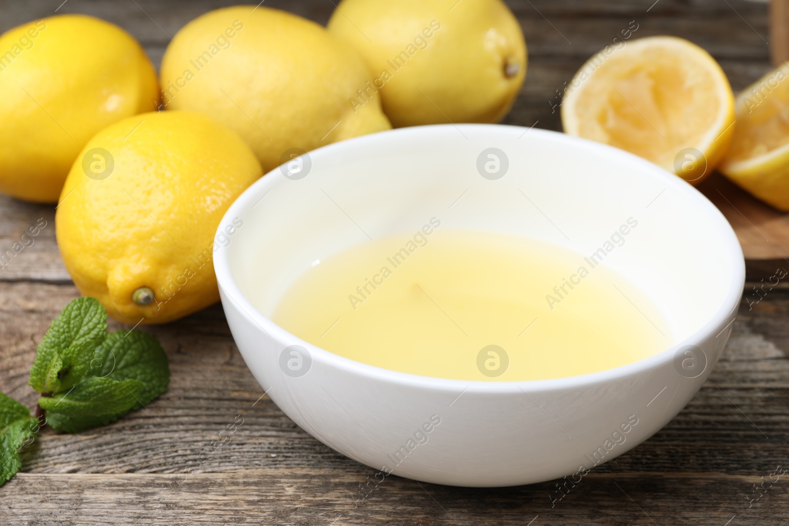 Photo of Fresh lemon juice in bowl and fruits on wooden table, closeup