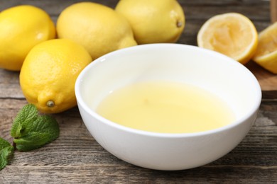 Photo of Fresh lemon juice in bowl and fruits on wooden table, closeup