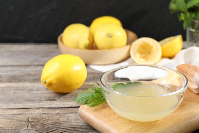 Fresh lemon juice in bowl and fruits on wooden table