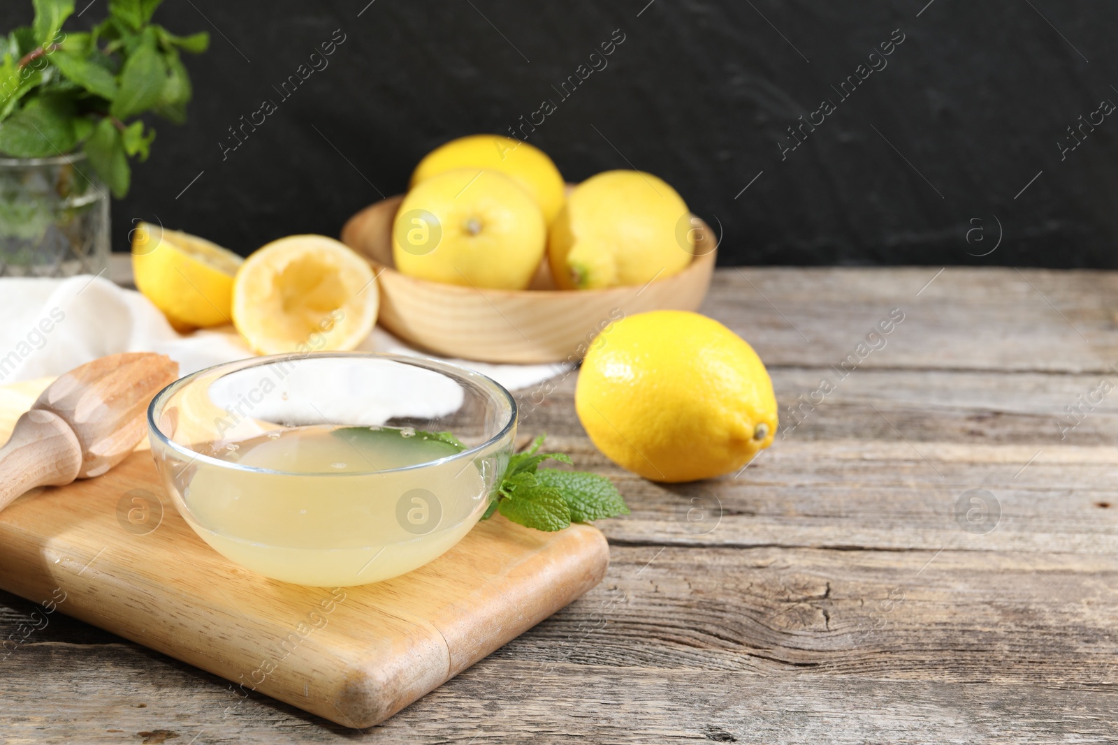 Photo of Fresh lemon juice in bowl, squeezer and fruits on wooden table