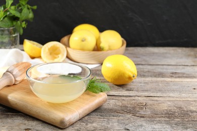 Photo of Fresh lemon juice in bowl, squeezer and fruits on wooden table