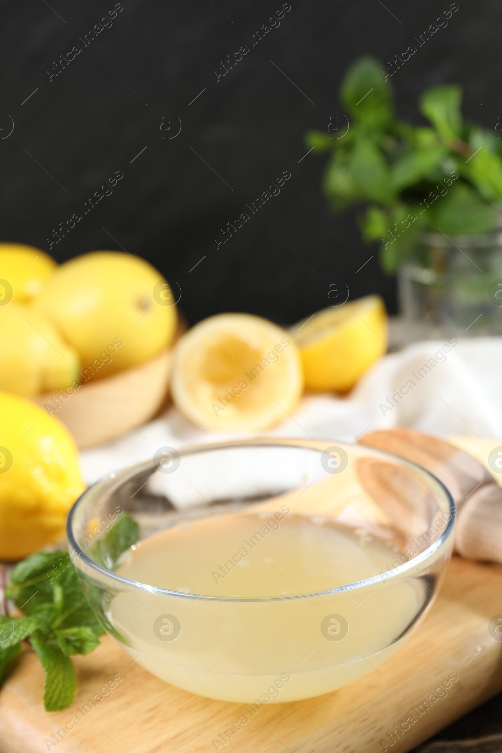 Photo of Fresh lemon juice in bowl and fruits on wooden table, closeup