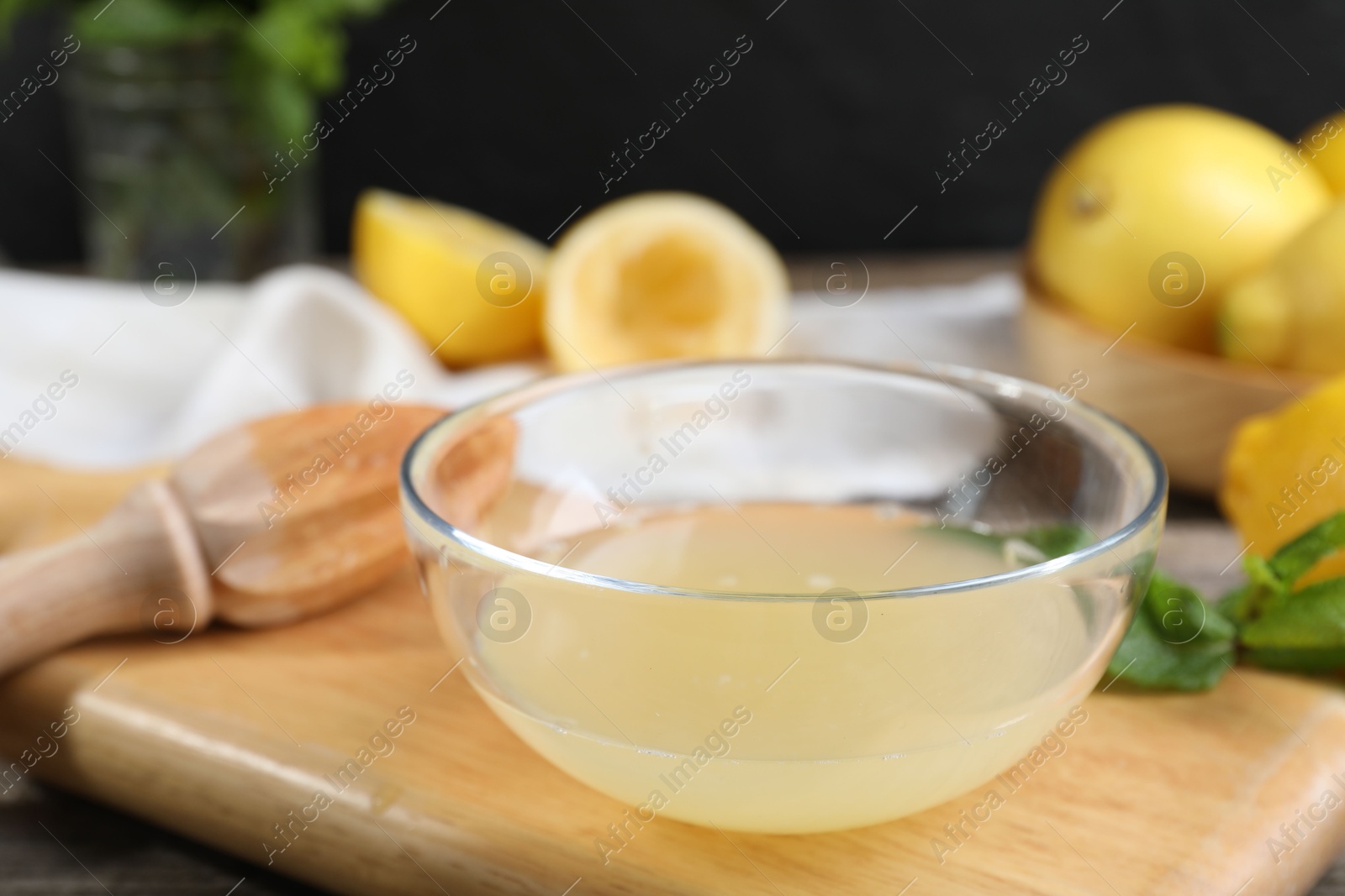 Photo of Fresh lemon juice in bowl, squeezer and fruits on wooden table, closeup