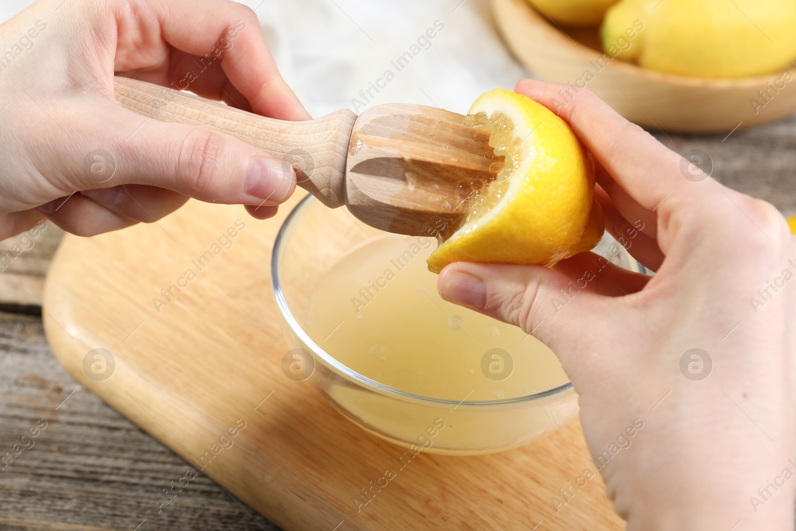 Photo of Woman juicing lemon into bowl at wooden table, closeup