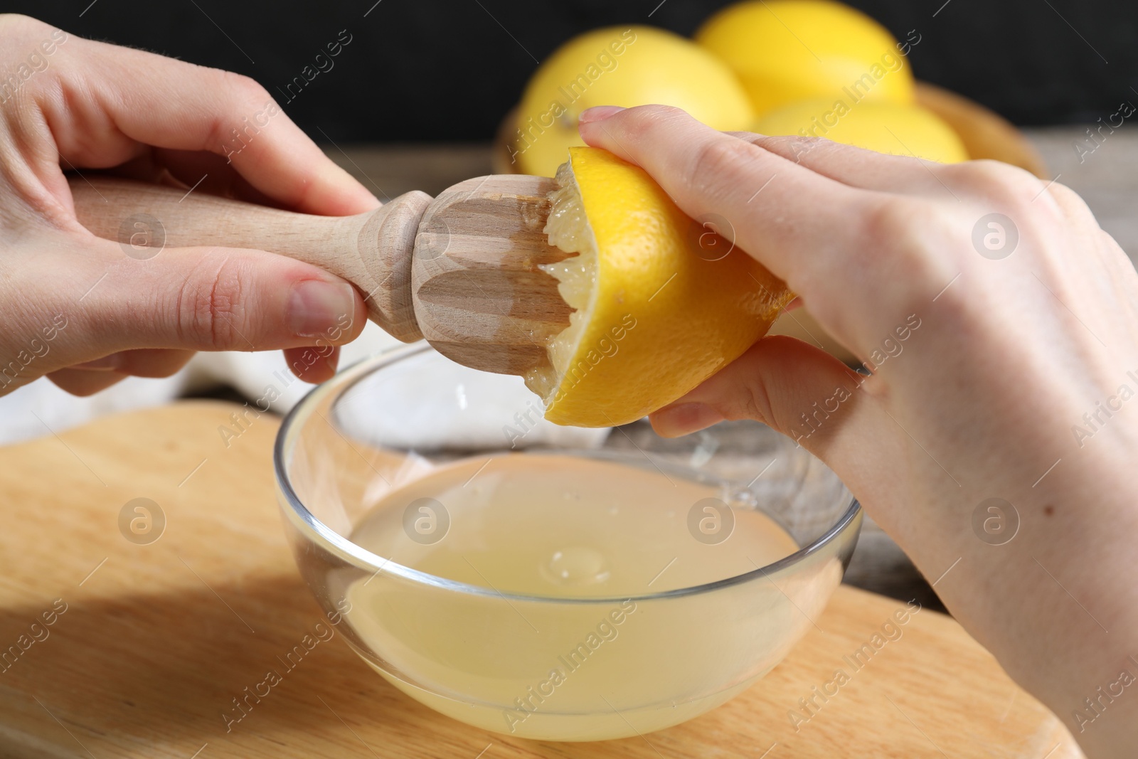 Photo of Woman juicing lemon into bowl at wooden table, closeup