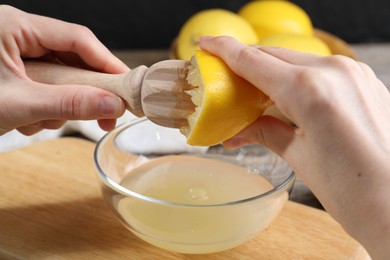 Photo of Woman juicing lemon into bowl at wooden table, closeup