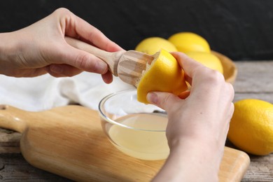 Woman juicing lemon into bowl at wooden table, closeup