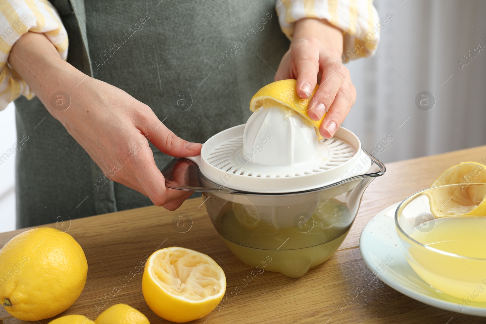 Photo of Woman with lemon using juicer at wooden table, closeup