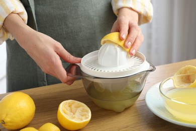 Photo of Woman with lemon using juicer at wooden table, closeup