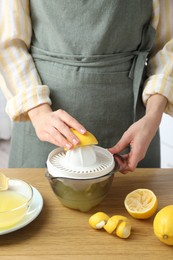 Photo of Woman with lemon using juicer at wooden table, closeup