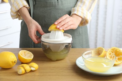 Woman with lemon using juicer at wooden table, closeup